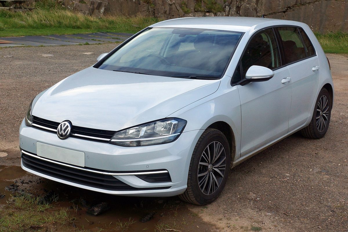 A white 2017 Volkswagen Golf five-door hatchback parked on muddy gravel beside a stone wall