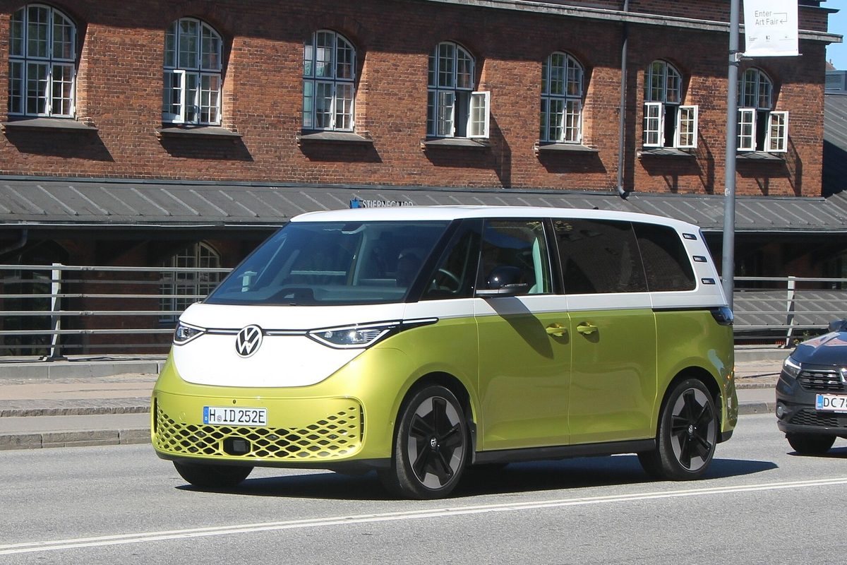 A two-tone lime green and white Volkswagen ID. Buzz minivan driving past a red brick building