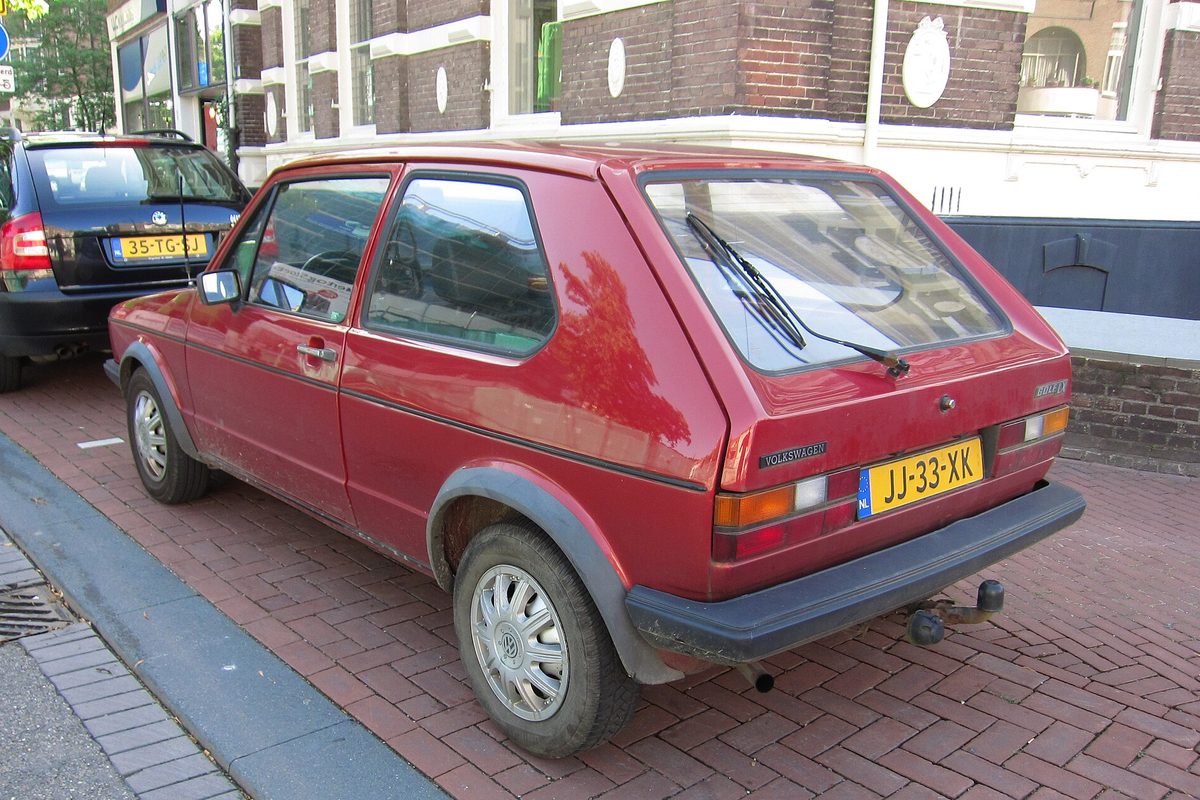 A red first-generation Volkswagen Golf hatchback, a 1983 diesel, seen from the rear corner while parked on a brick street in Nijmegen, the Netherlands