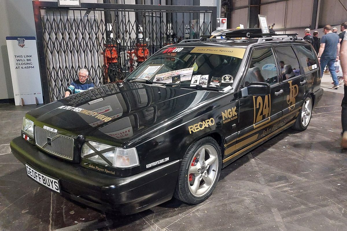 A black Volvo 850 wagon in black and gold race-style livery with sponsor decals, parked indoors at a car show