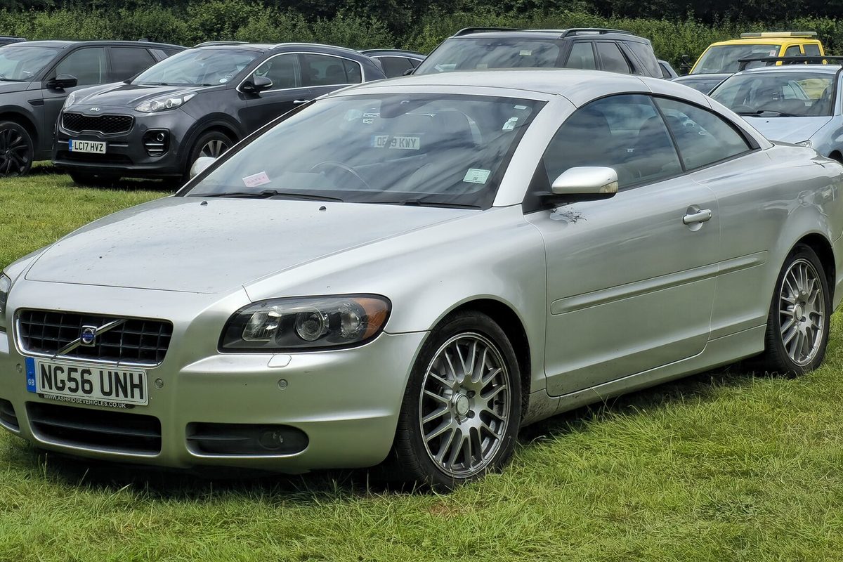 A silver second-generation Volvo C70 with its roof up and multi-spoke alloy wheels, parked on grass at an outdoor car park