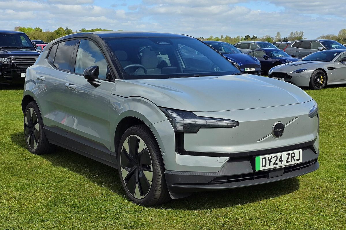 A pale sage-green Volvo EX30 small electric SUV parked on grass at an outdoor car show