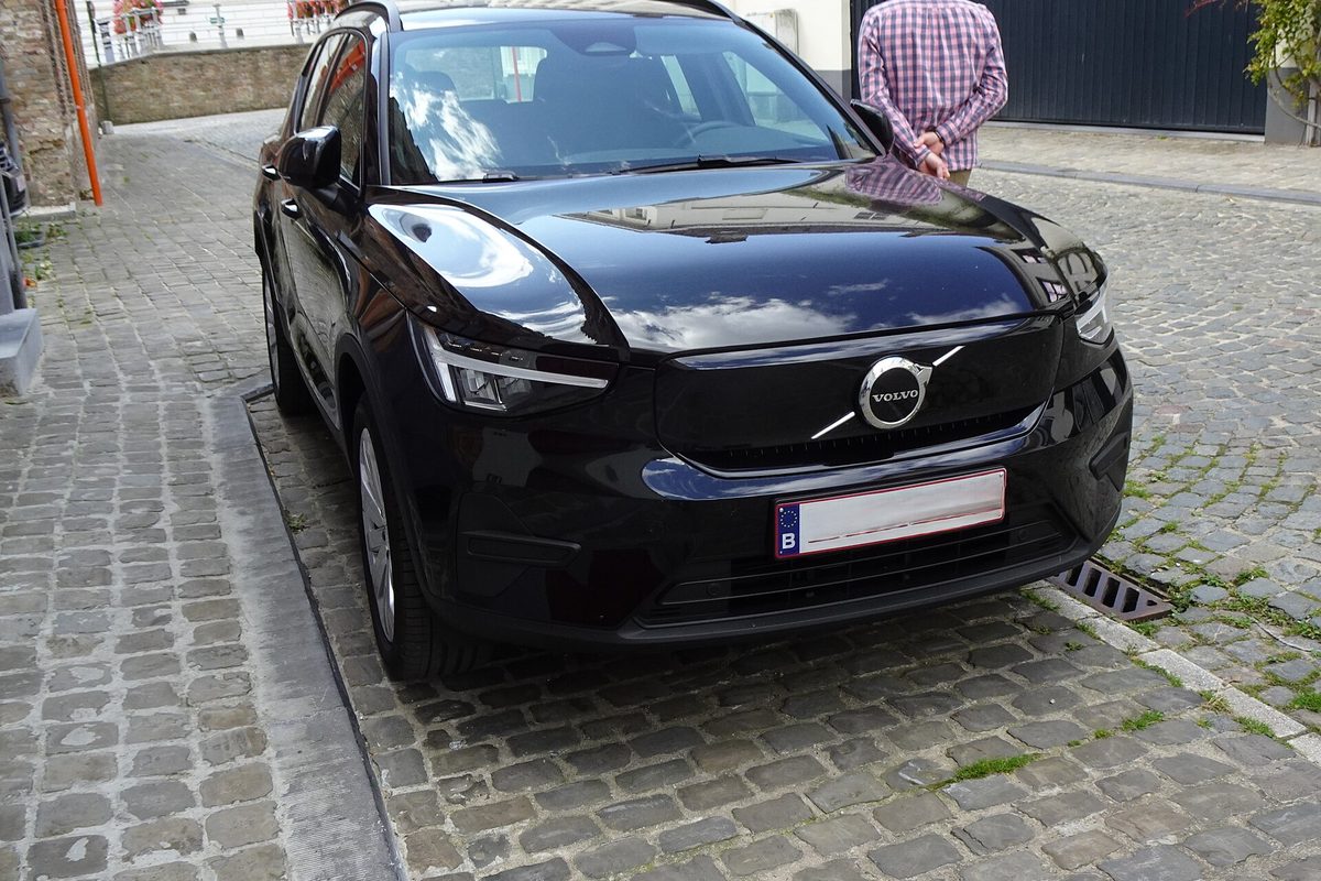 A black Volvo EX40 small electric SUV parked on a cobblestone street, seen from the front, with a man standing behind it