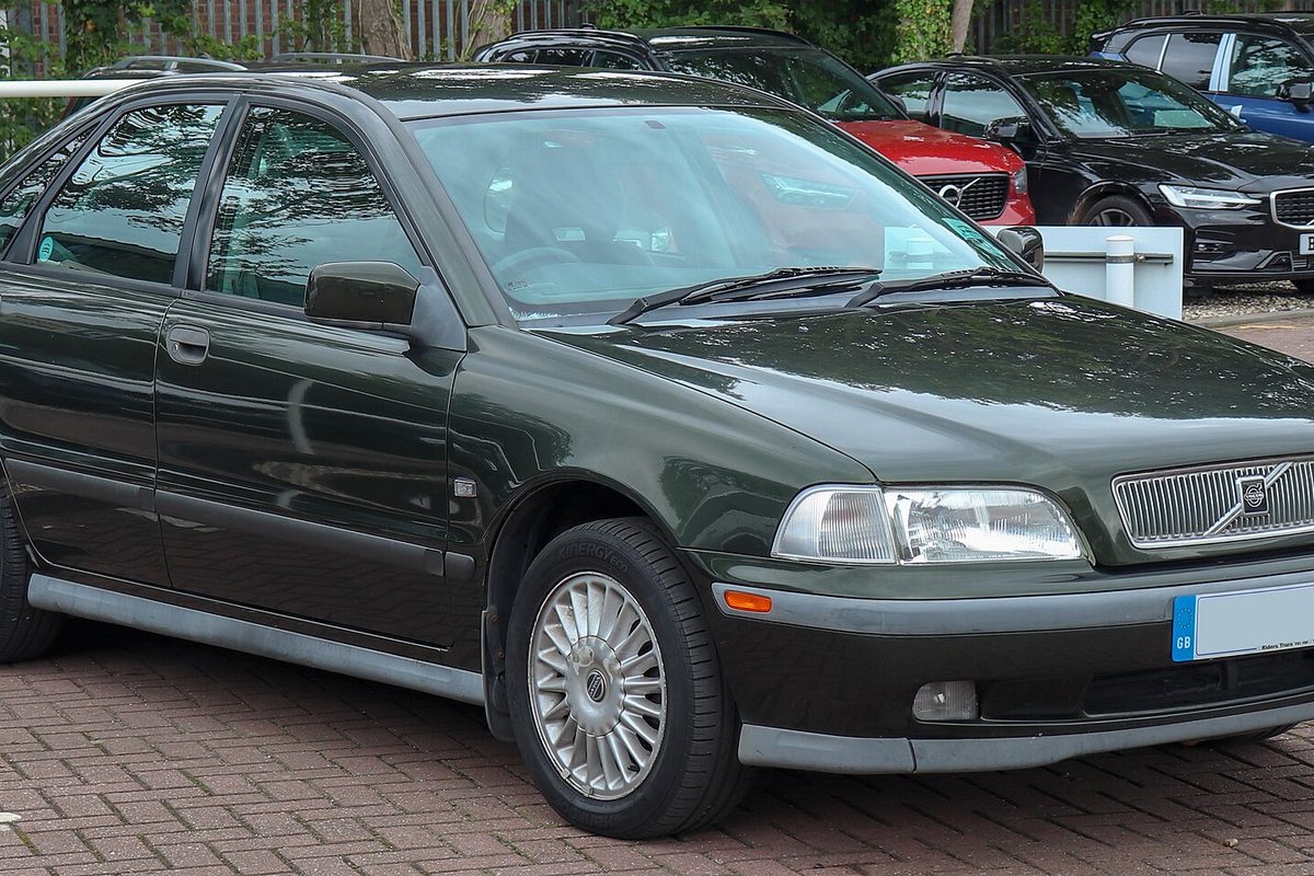 A dark green first-generation Volvo S40 sedan with silver alloy wheels, parked on a brick-paved lot