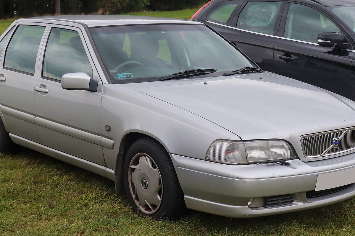 A silver 1999 Volvo S70 sedan with plastic wheel covers, parked on grass