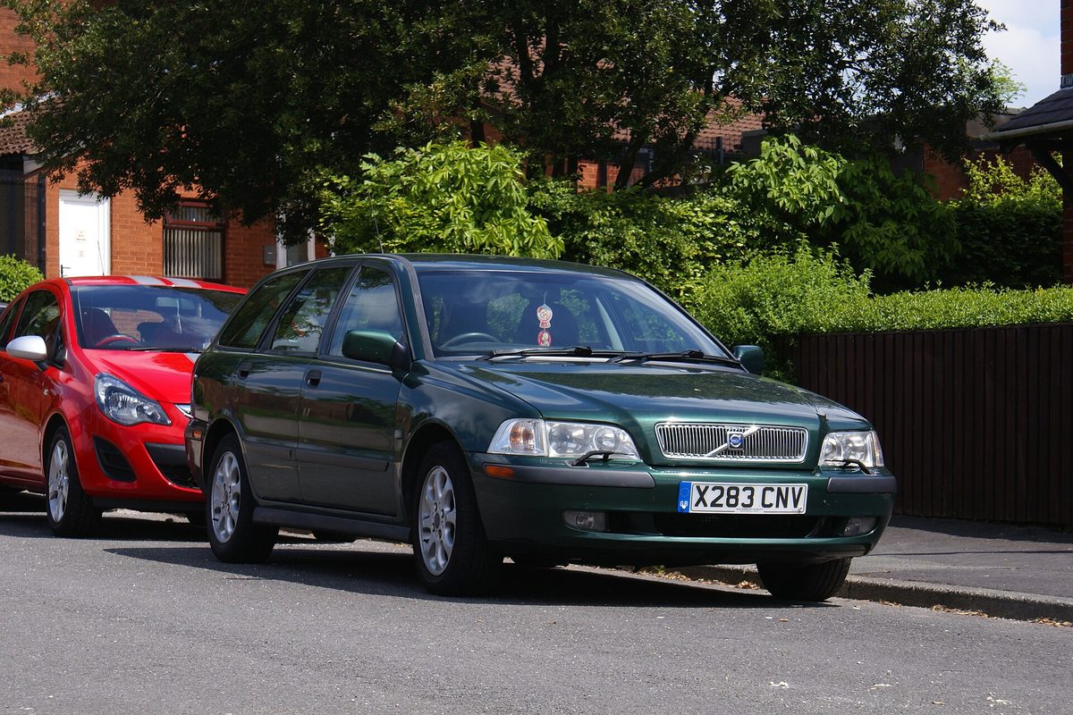 A dark green 2000 Volvo V40 wagon parked on a residential street in front of a red hatchback