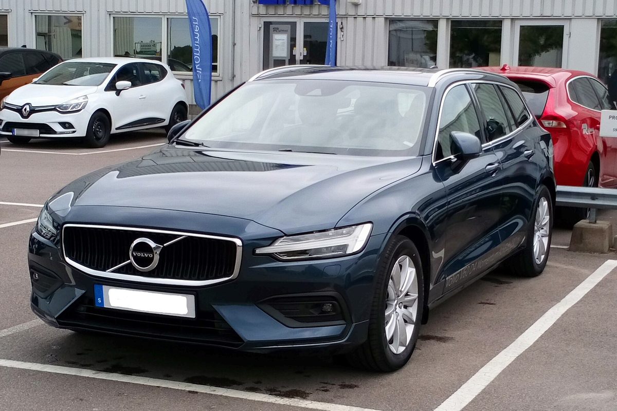 A dark blue 2018 Volvo V60 wagon parked in a dealership lot, with a white hatchback and a red car beside it
