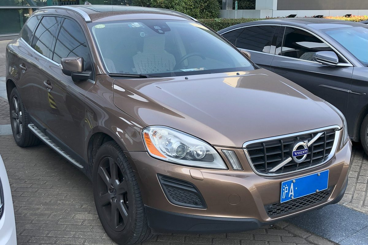 A bronze Volvo XC60 SUV with dark wheels and side steps, parked on paving stones beside a gray car