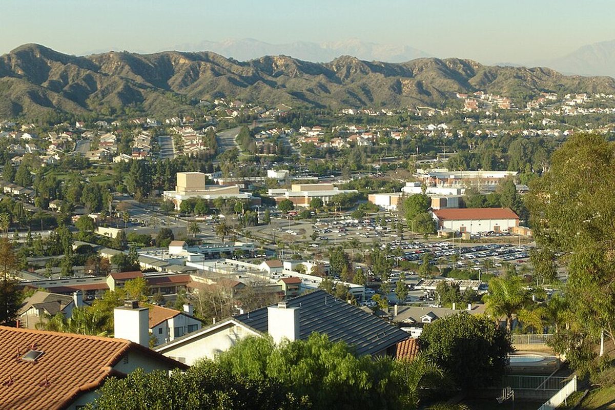 A view from a Walnut hillside over red tile roofs to the Mt. San Antonio College campus and its parking lots, with green hills behind
