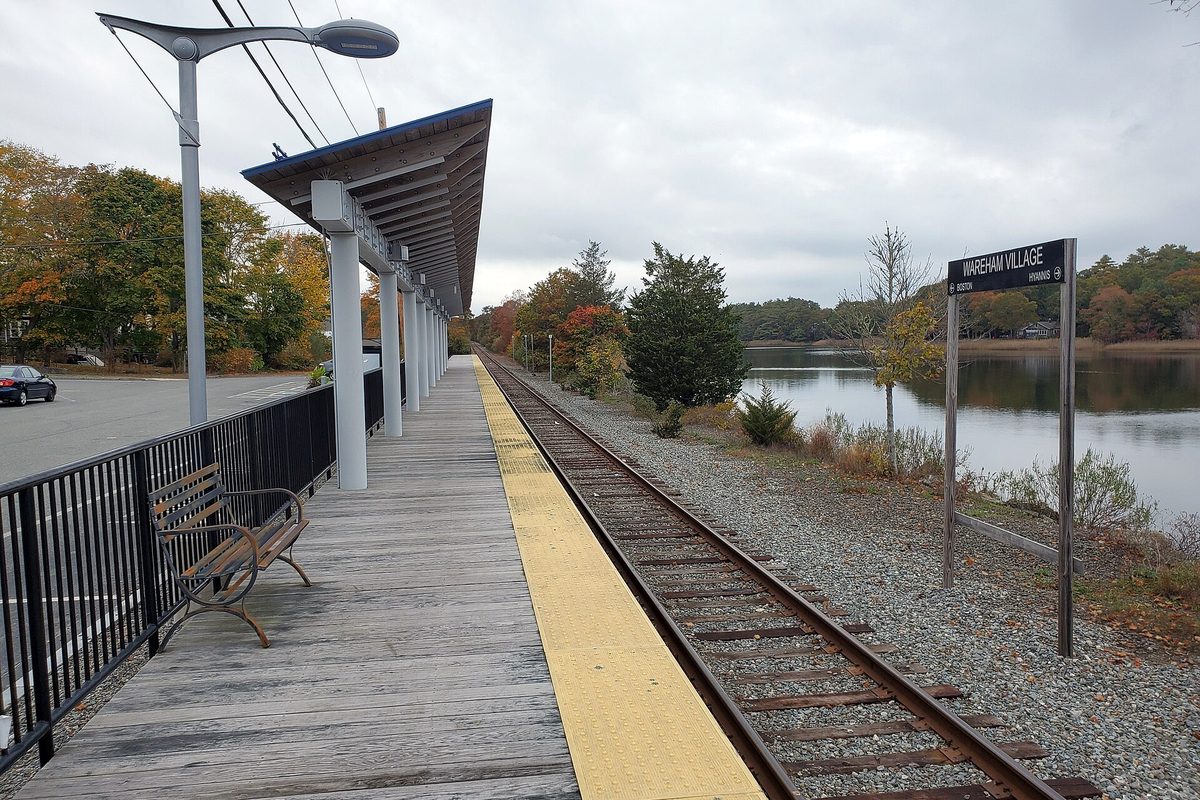 The wooden platform of Wareham Village station beside the rail line, with a pond and autumn trees beyond the tracks