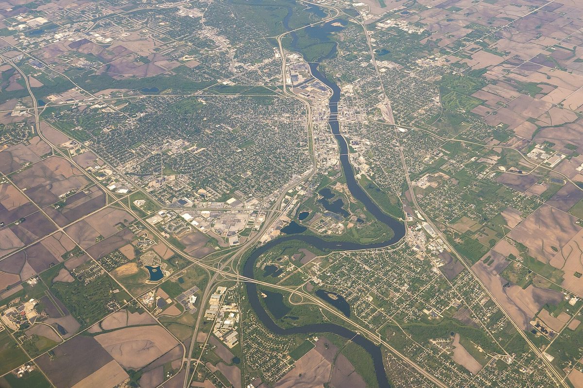 Aerial view of Waterloo from high above, a river curving through the middle of the city with neighborhoods and highways on both banks and farm fields around the edges