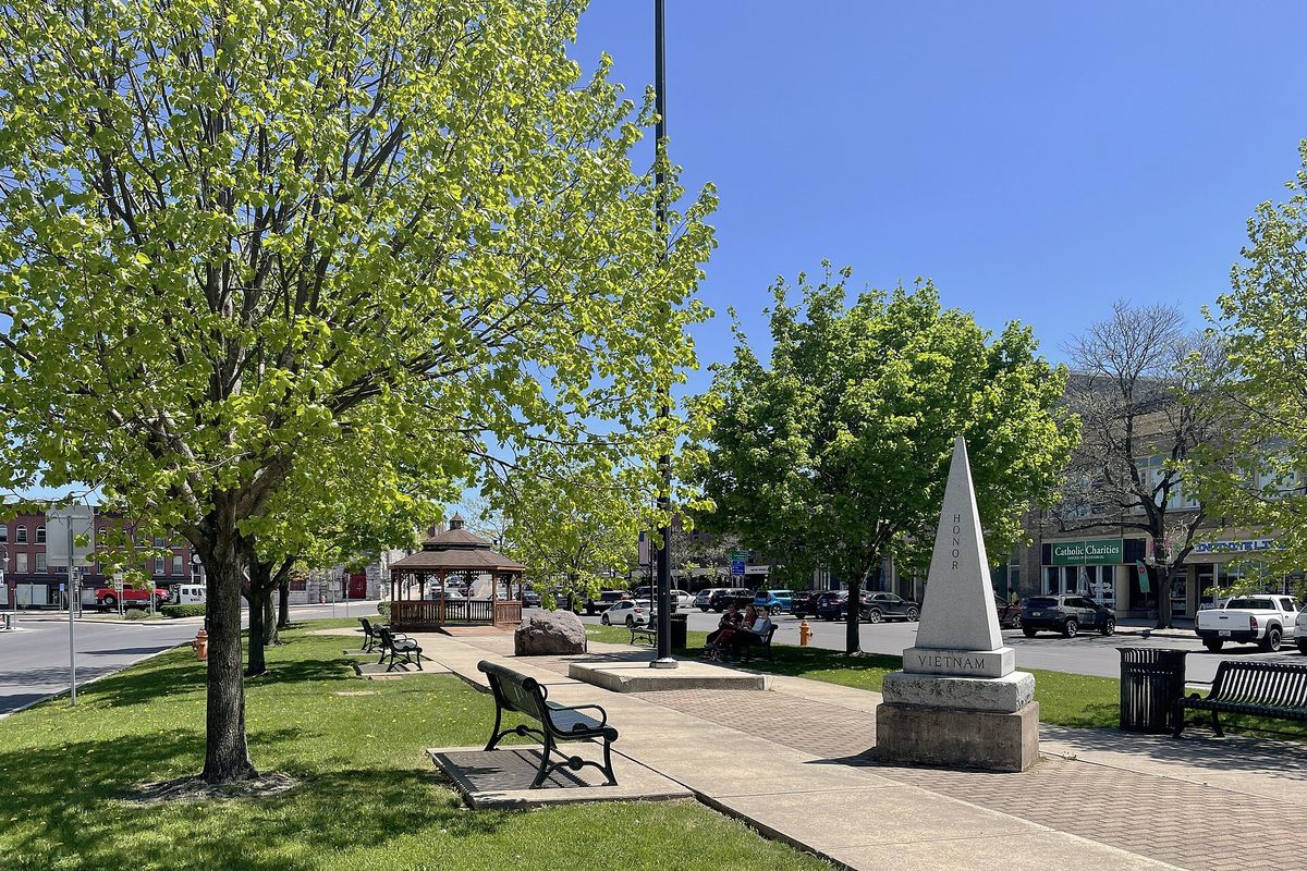 Public Square in Watertown in spring, with a white Vietnam memorial obelisk, park benches, a gazebo and young trees in new leaf