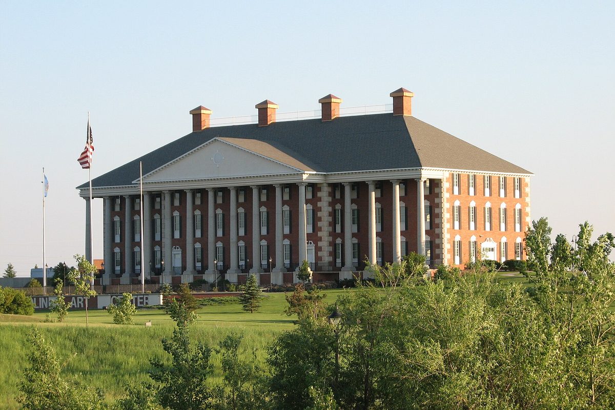 The Redlin Art Center in Watertown, a red-brick building with tall white columns and brick chimneys on a grassy rise, an American flag out front