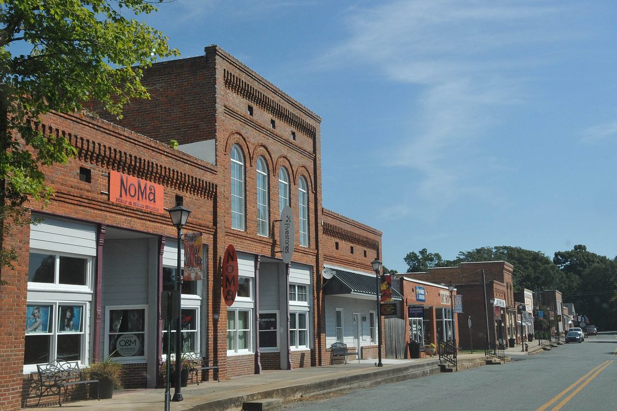 A row of early 20th-century brick storefronts with arched upper windows along a main street in Waxhaw's historic district, with street lamps and a bench
