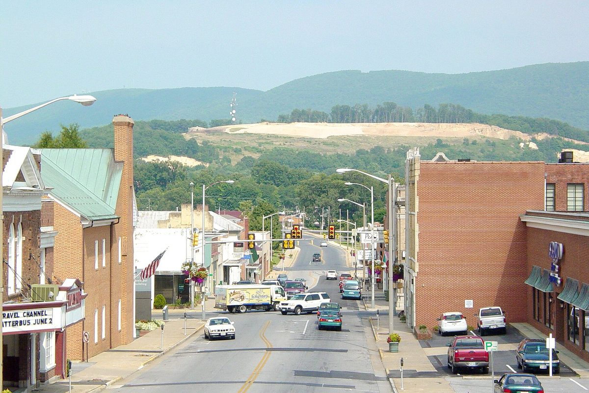 Main Street in downtown Waynesboro looking toward a green mountain with a bare scar on its slope, brick storefronts on both sides and the Wayne Theater at far left