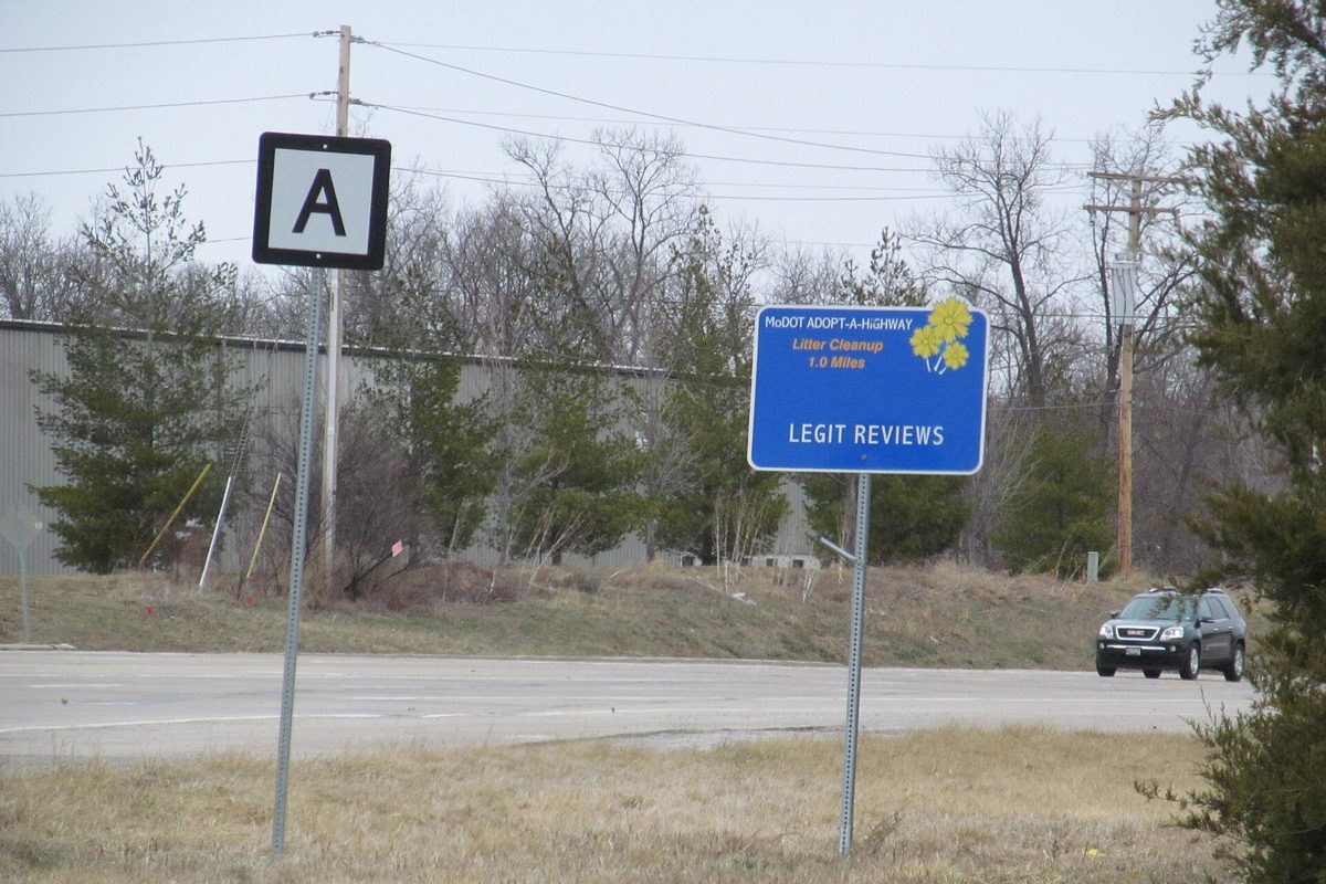 A MoDOT Adopt-a-Highway litter cleanup sign and a Route A marker beside Wentzville Parkway, with bare trees and an SUV passing