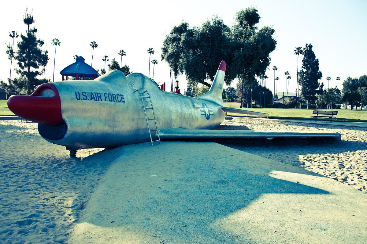 A retired silver F-86 Sabre fighter jet marked U.S. Air Force, set on sand as play equipment in a park lined with palm trees