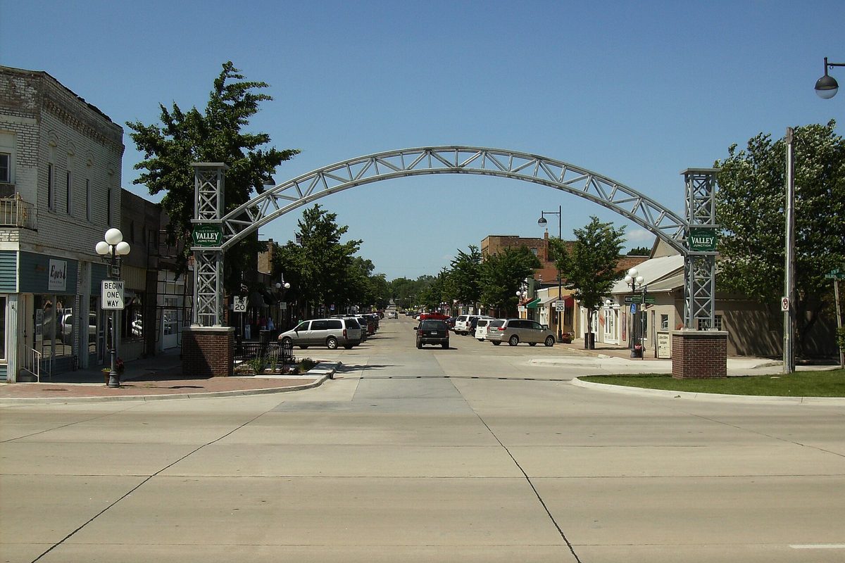 The steel arch over the street at Historic Valley Junction in West Des Moines, with brick storefronts and parked cars on a sunny day