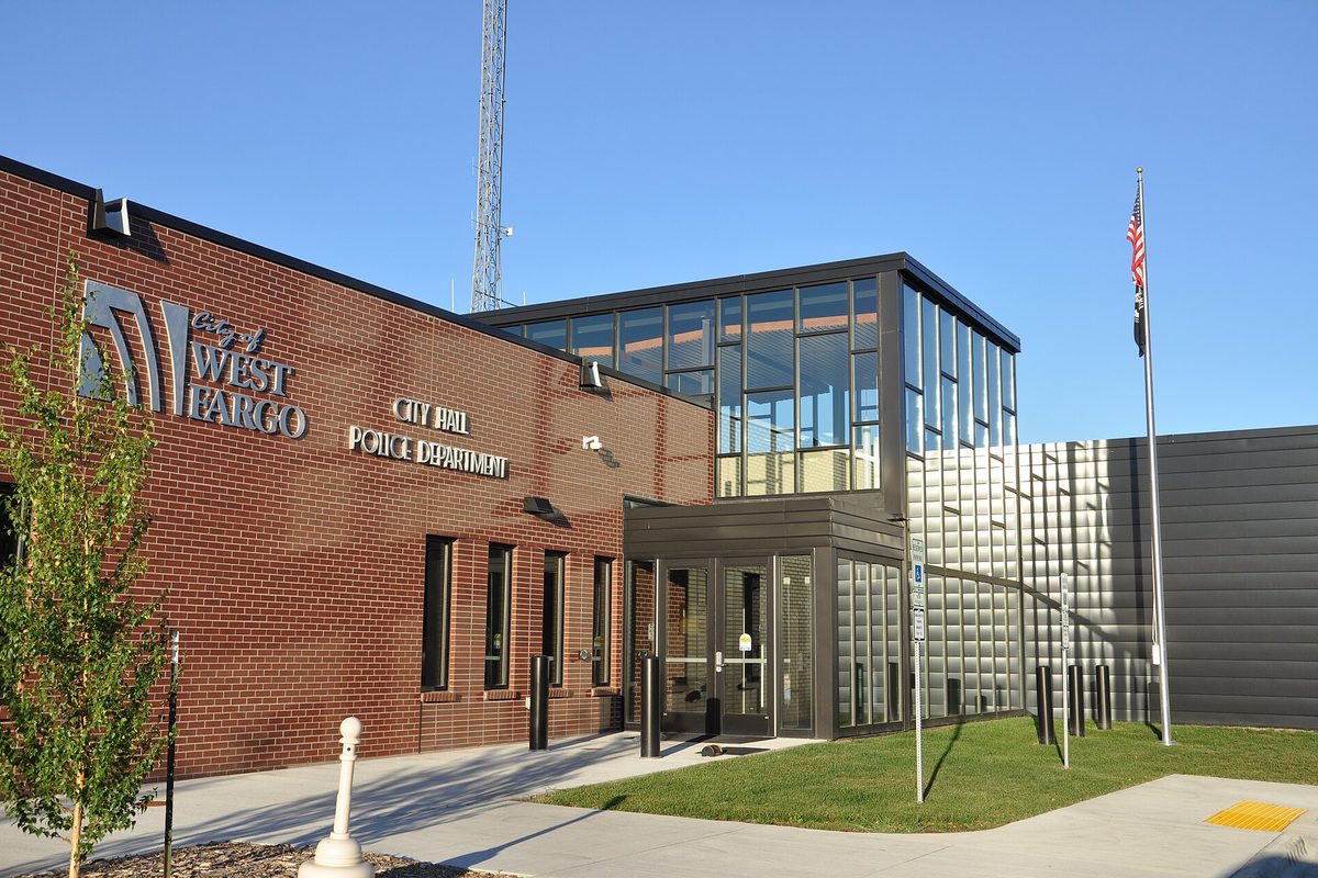 West Fargo City Hall and Police Department, a red brick building with a glass entrance and a flagpole under a clear blue sky