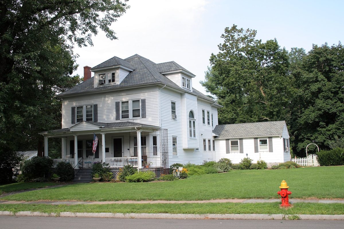 The Edward W. Morley House in West Hartford, a white two-and-a-half-story house with a hip roof, a front porch with an American flag, a green lawn and a red fire hydrant at the curb