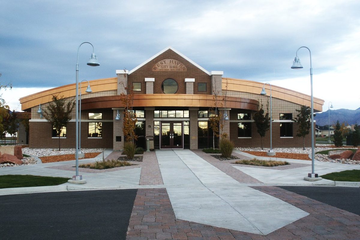 West Haven City Hall, a curved brick and tan building with a round window over glass doors, a paved walkway lined with lamp posts and mountains in the distance