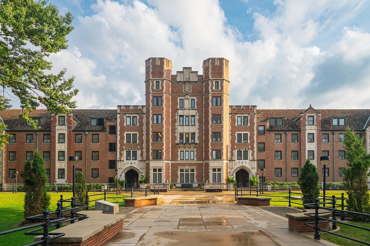Cary Quadrangle at Purdue University, a red-brick residence hall with twin square towers, seen across a wet paved courtyard with trees