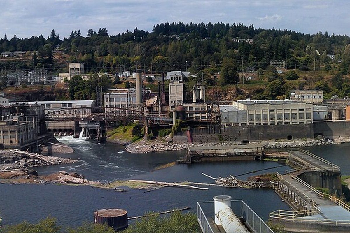 Willamette Falls and the old riverside mill buildings, looking west toward the wooded hills of West Linn
