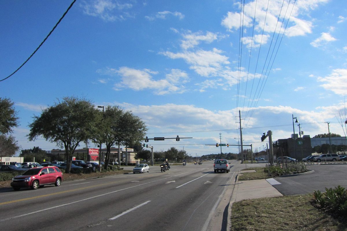 Wickham Road near New Haven Road in West Melbourne, a wide road with a red SUV, a white pickup and motorcycles under tall power lines and a blue sky