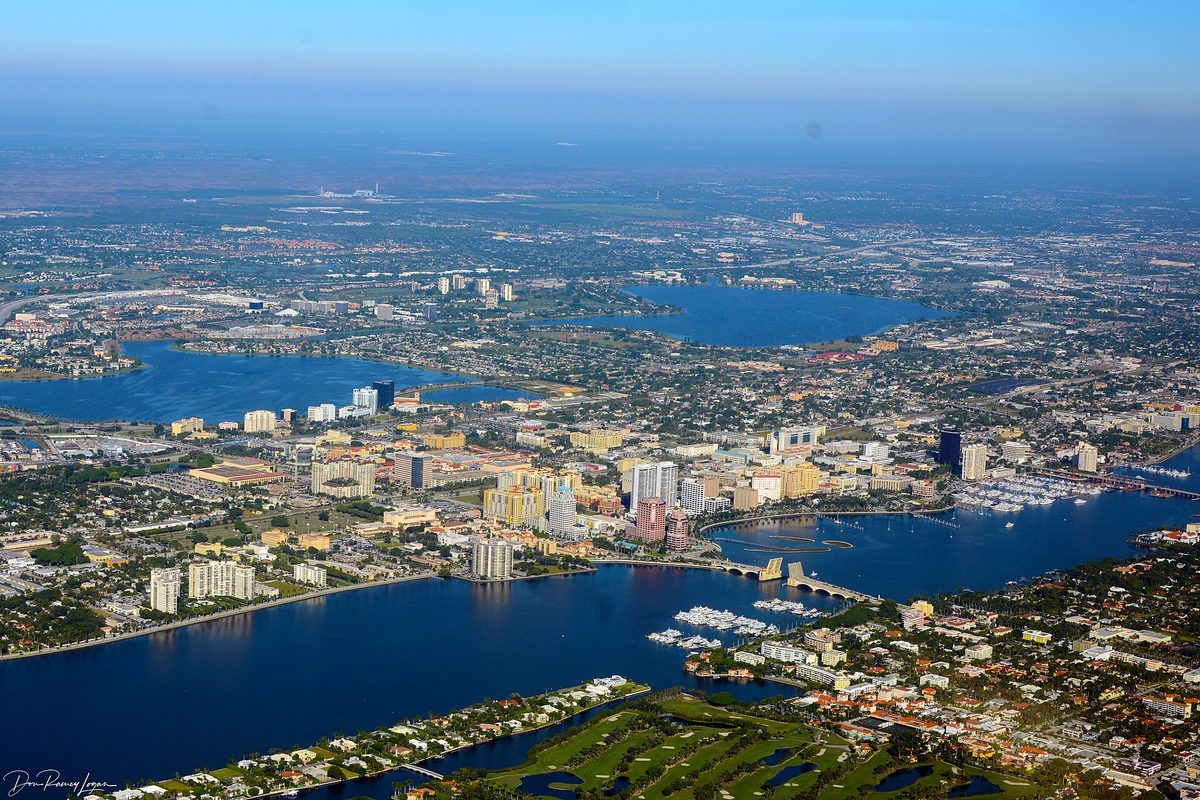 Aerial view of downtown West Palm Beach towers along the Intracoastal Waterway, with bridges, boat marinas and inland lakes stretching west