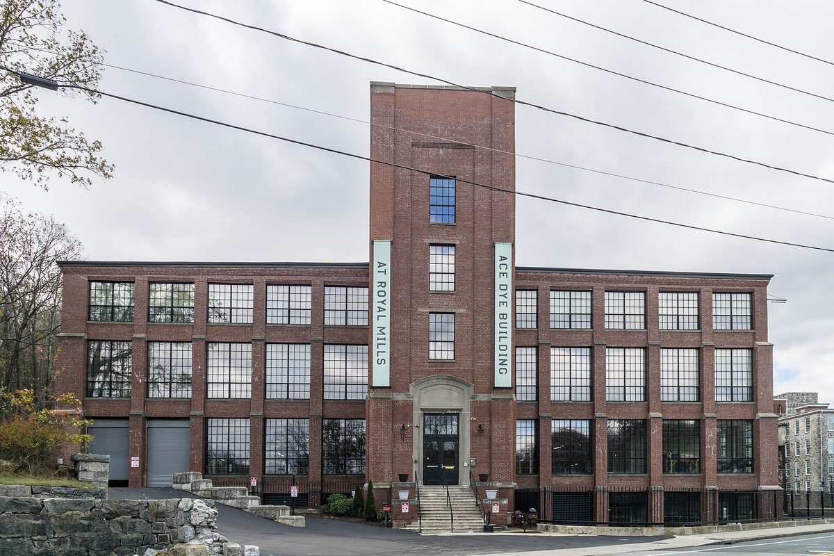 The four-story red brick Ace Dye Building at Royal Mills in River Point, with a tall central tower and two vertical banners on its front