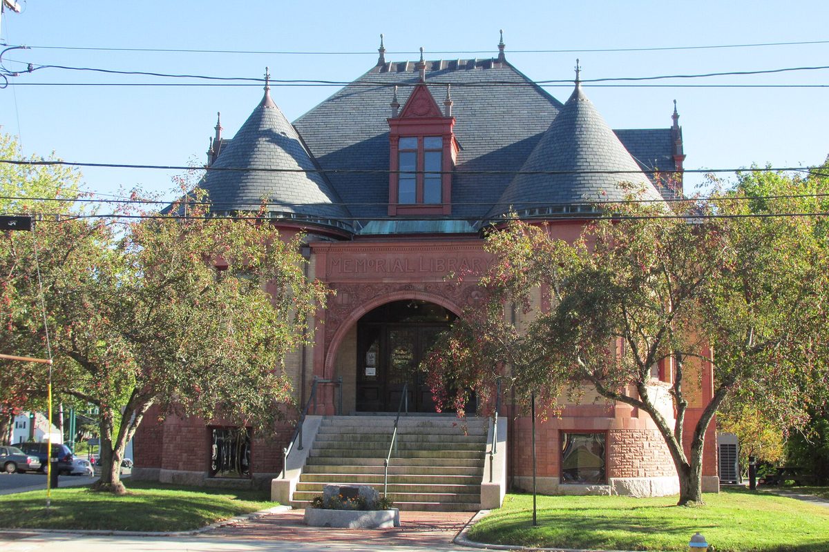 Walker Memorial Library in Westbrook, a red sandstone building with round slate-roofed turrets and an arched entrance, framed by autumn trees