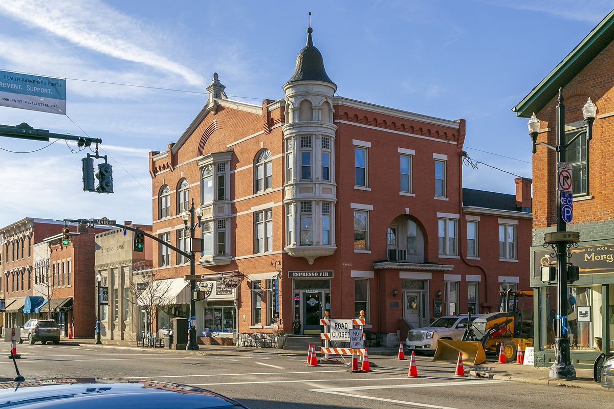 The red brick Holmes Hotel building in Westerville, with a rounded corner bay topped by a small dome, behind orange traffic cones and a small excavator on the street