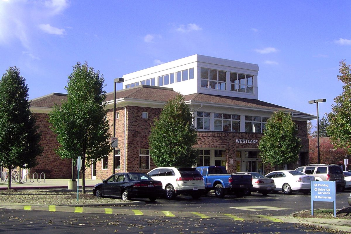 The Westlake Porter Public Library, a brick building with a white glass-walled top story, cars and a blue pickup parked in the lot in front