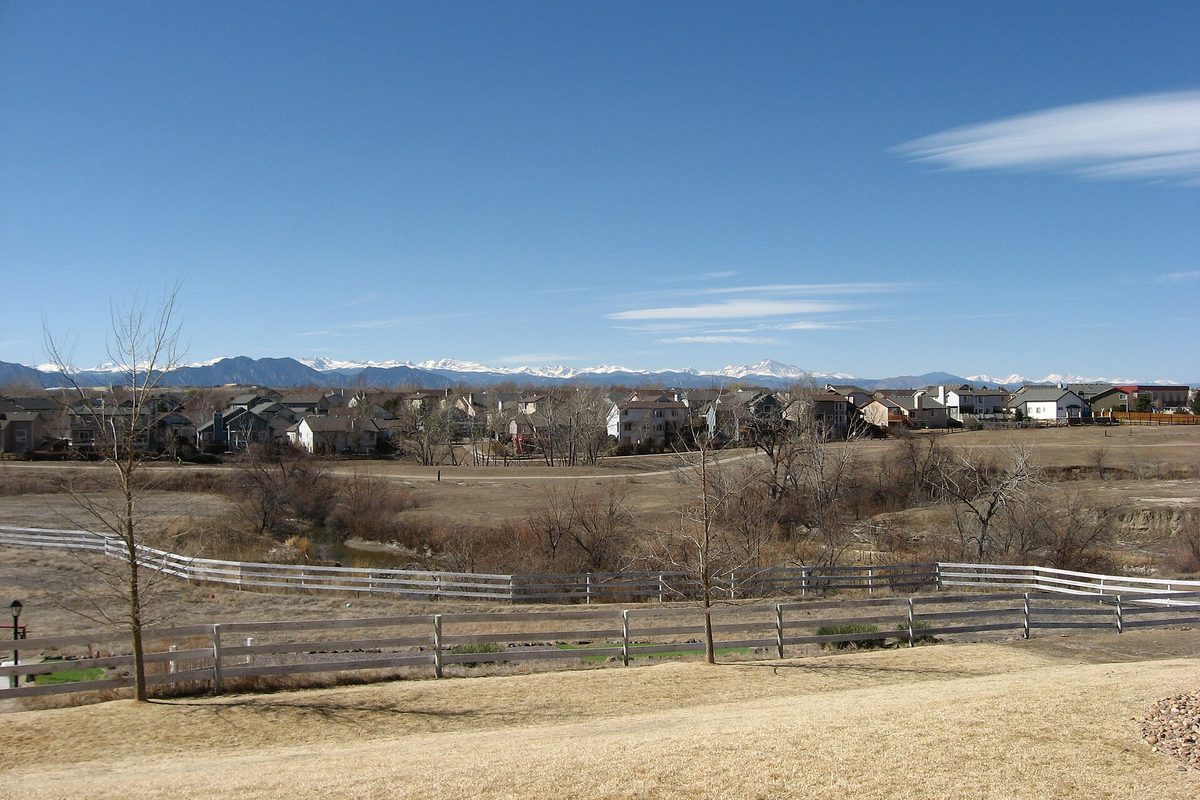 Houses in northeastern Westminster seen across a fenced, dry open field, with snow-capped Rocky Mountains along the horizon