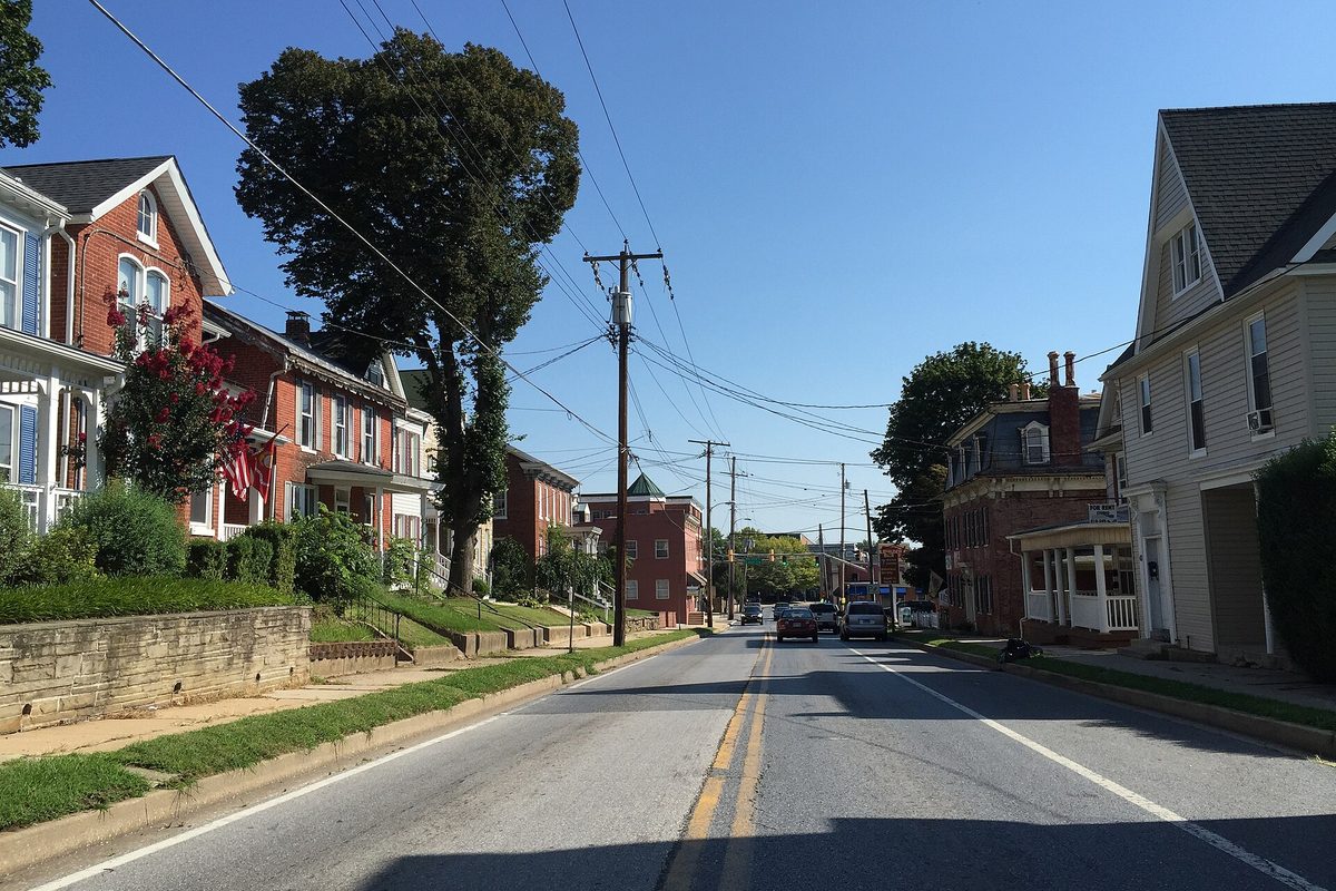 Liberty Street in Westminster looking north past brick and frame houses, a large shade tree and utility poles under a clear blue sky