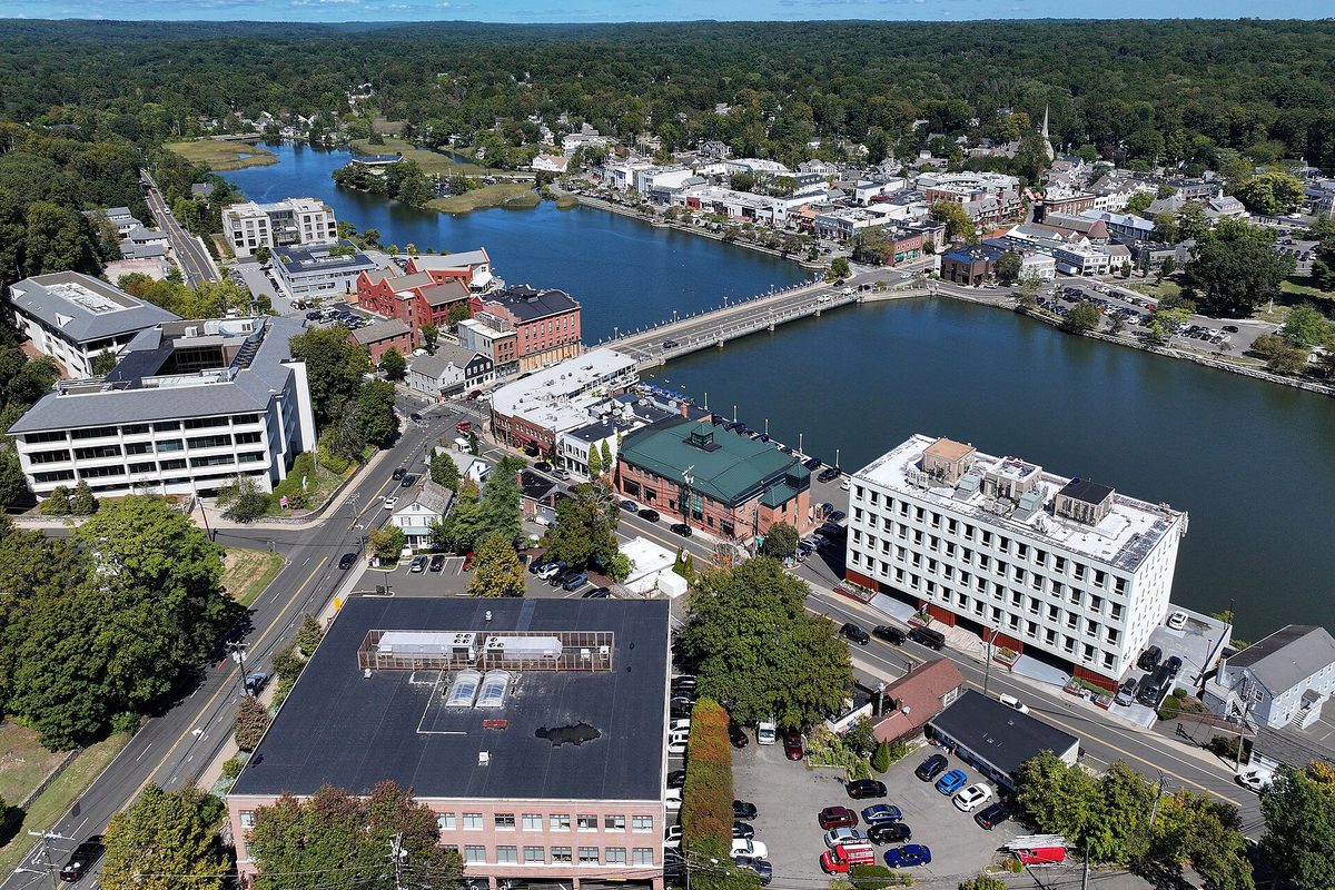 Aerial view of downtown Westport, where a bridge crosses a wide river between brick and white buildings, with trees to the horizon