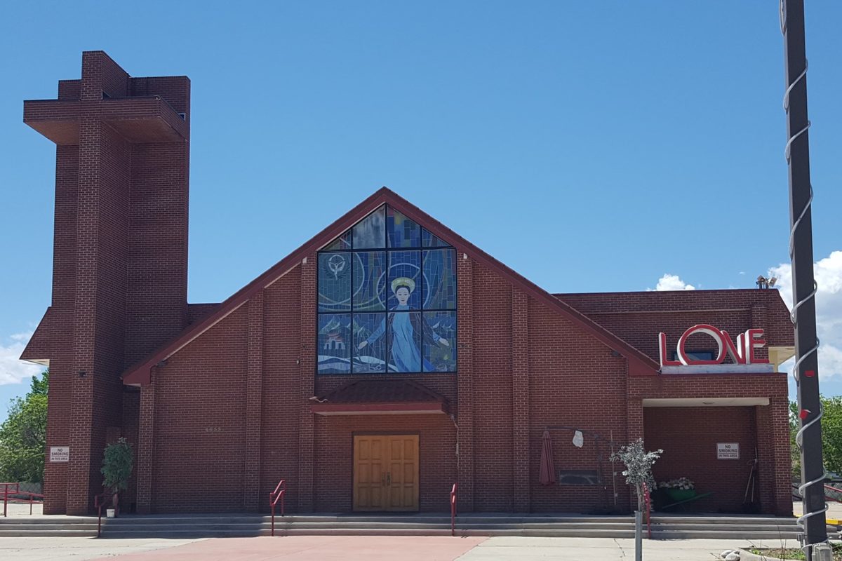 Queen of Vietnamese Martyrs Catholic Church in Wheat Ridge, a brick building with a tall stained-glass window of a robed figure, a square tower and a red LOVE sign