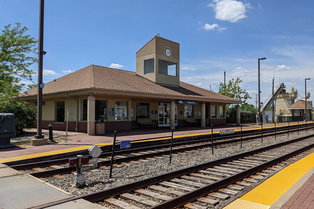 The tan Wheeling Metra station with its clock tower, seen across the tracks and platform on a sunny day
