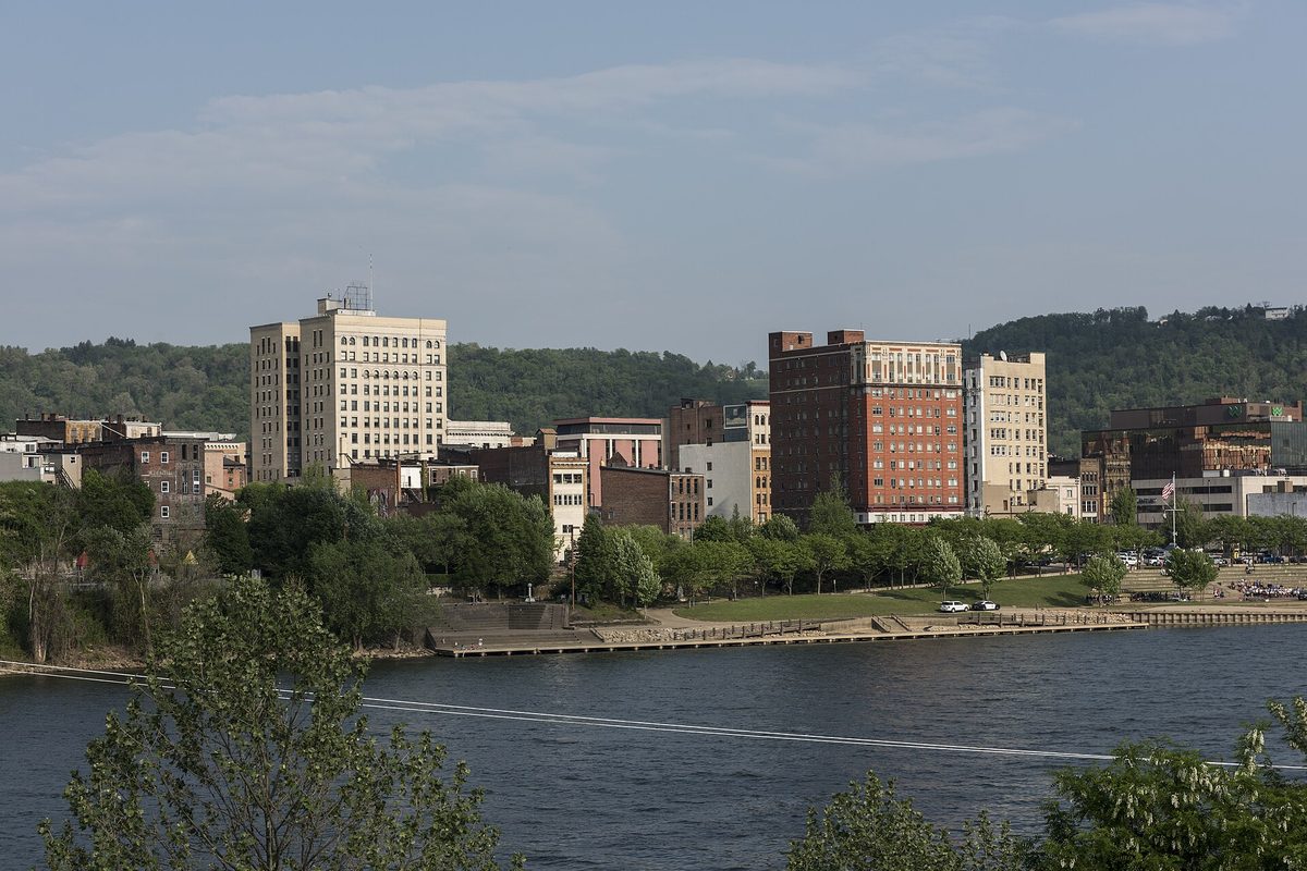 Downtown Wheeling's brick and stone high-rises along the Ohio River waterfront, seen from Wheeling Island, with wooded hills behind