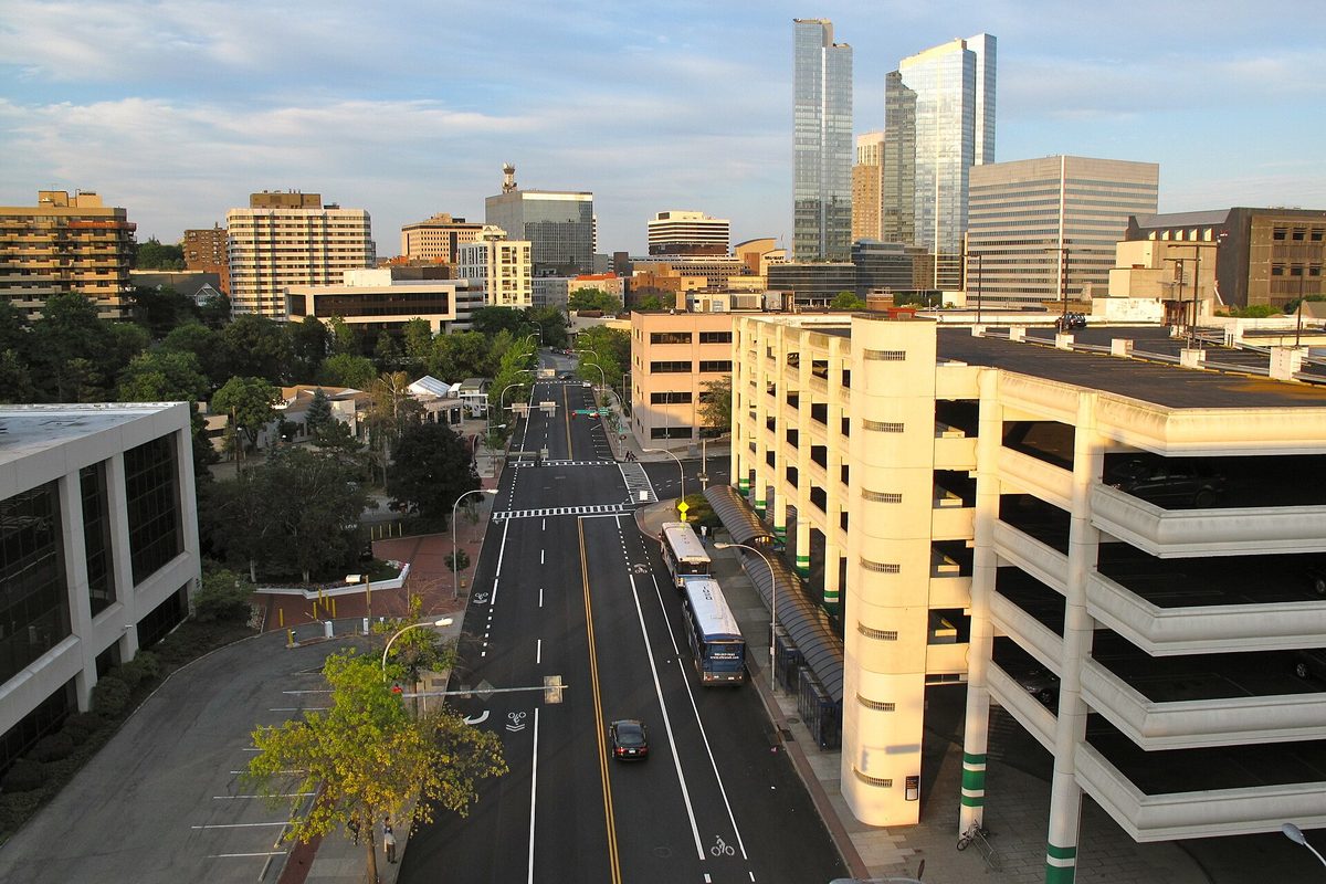 Downtown White Plains from above: glass office towers and apartment blocks behind a wide avenue, with two buses beside a tall parking garage