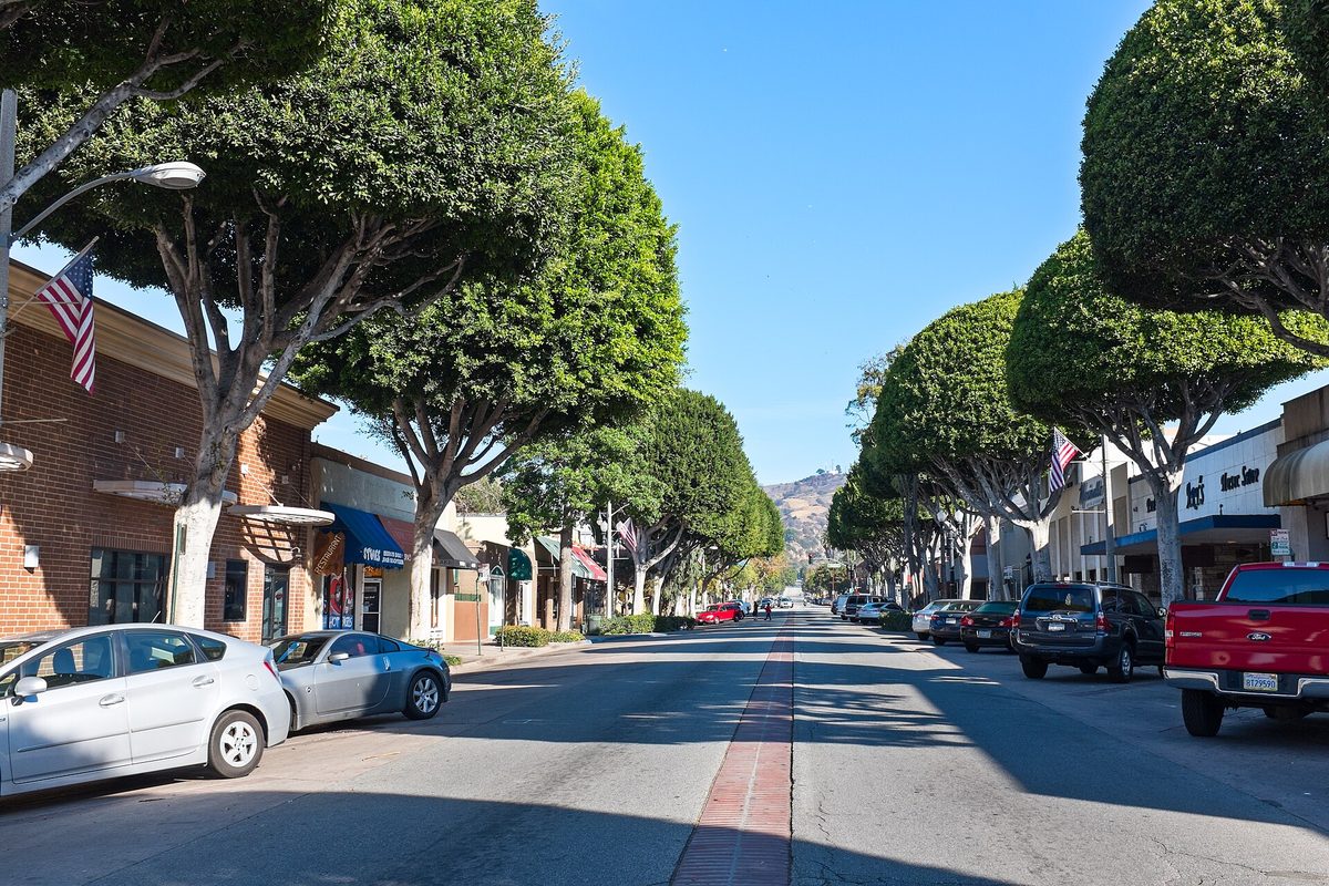 Greenleaf Street in uptown Whittier, rounded trees shading brick storefronts and parked cars, with a hill at the far end of the street