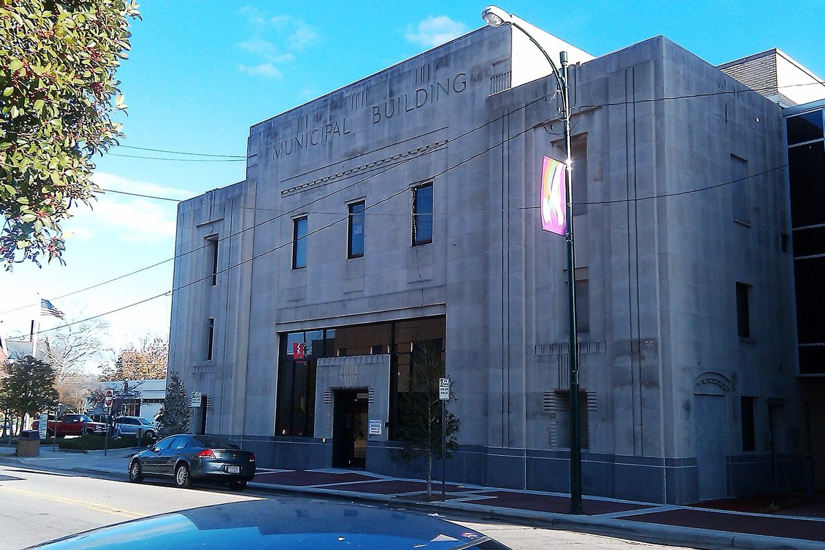 The pale stone Municipal Building in Wilson, North Carolina, with its name carved above the windows, a banner on a lamppost and a car parked at the curb