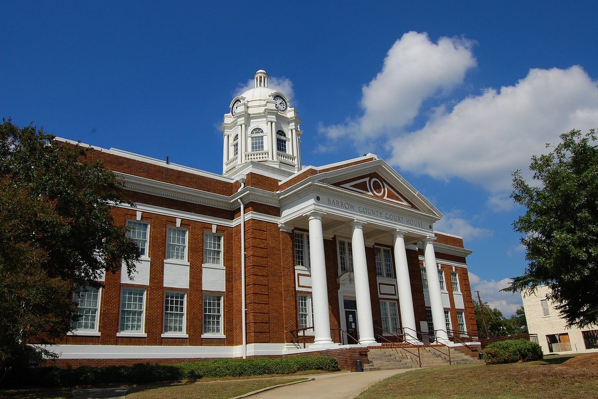 The Barrow County Courthouse in Winder, a red-brick building with tall white columns and a white domed clock tower against a blue sky