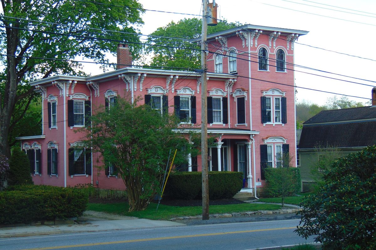 The Laura Huntington House in Windham Center, a pink Italianate house with black shutters and ornate white window trim, behind shrubs beside a road