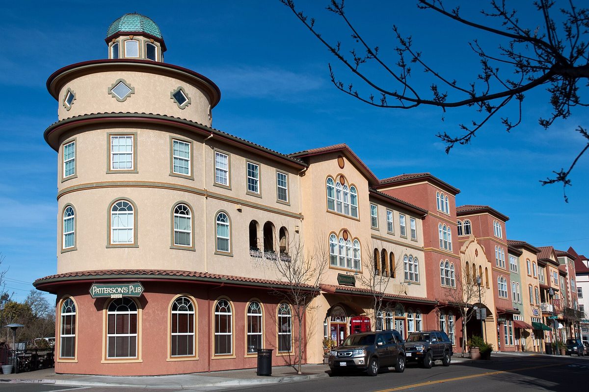 A curved, domed corner building with arched windows on a street in downtown Windsor, home to Patterson's Pub, with two SUVs parked out front under a blue sky
