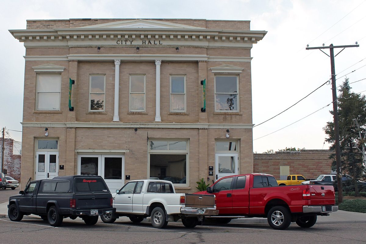 The two-story tan brick Windsor Town Hall on 5th Street, lettered City Hall above the windows, with a black, a white and a red pickup parked out front