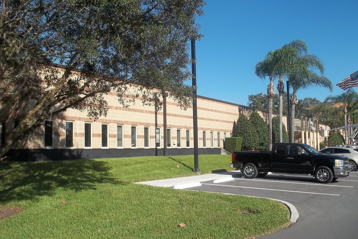 Winter Springs City Hall, a long tan brick building with rows of tall windows, with palm trees, an American flag and a black pickup in the parking lot