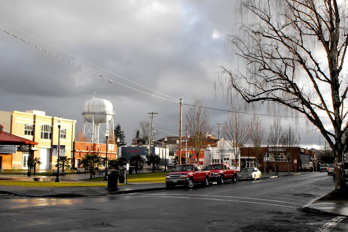 Woodburn's central square on a wet day, with a white water tower, red pickup trucks and bare trees under storm clouds