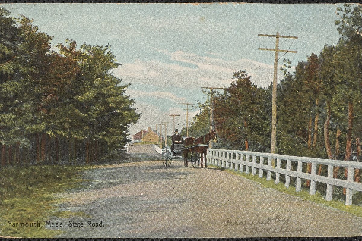 An old tinted postcard of State Road in Yarmouth, with a horse and buggy on a dirt road between tall trees and a white wooden fence