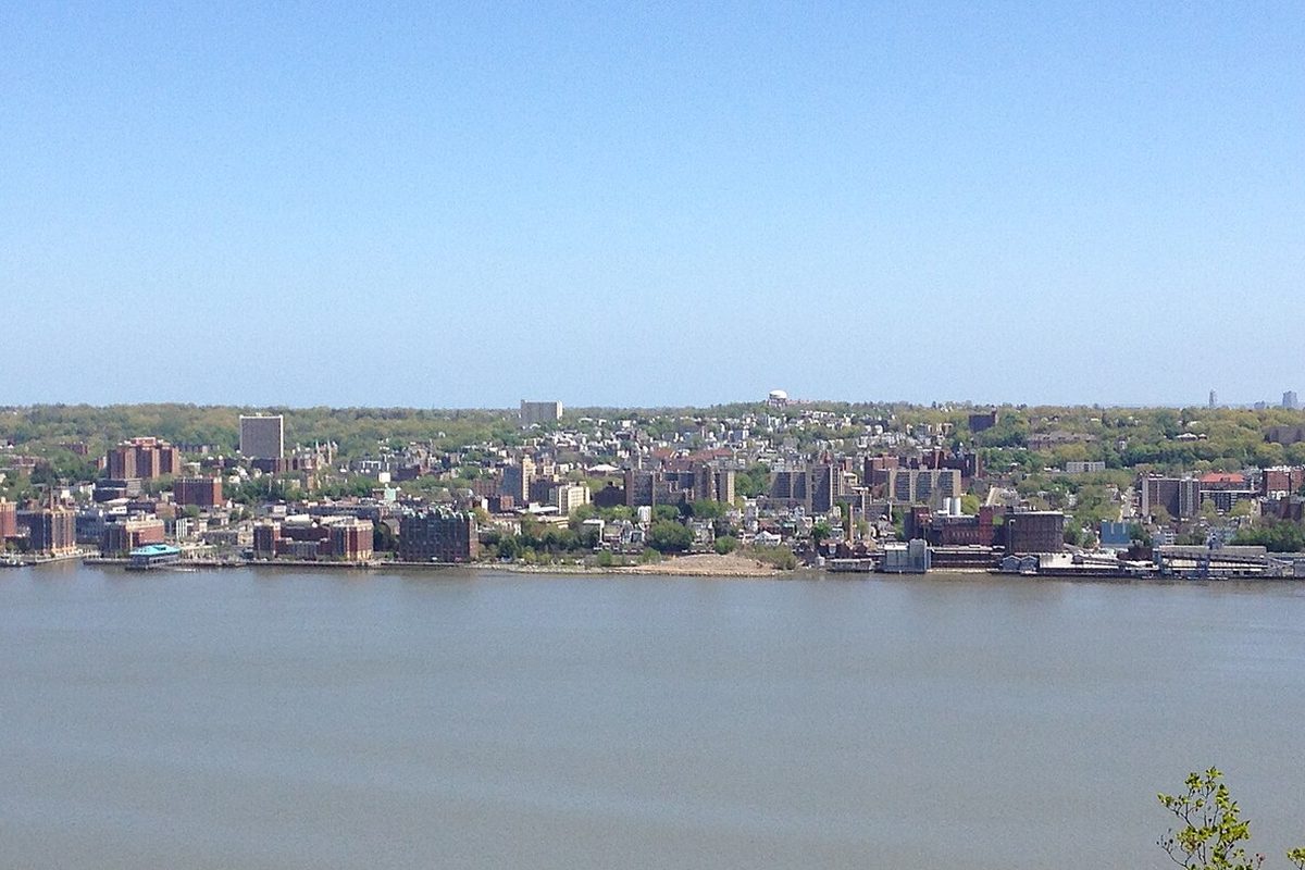 Yonkers spread along the Hudson River shoreline under a clear sky, seen across the water from the New Jersey Palisades